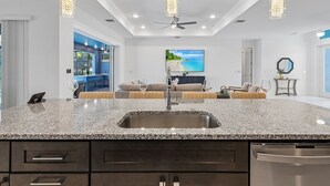 A modern kitchen with granite countertops, a stainless steel sink, and a built-in dishwasher. - GULF ACCESS & BIG WATER VIEW!, Heated Saltwater Pool  and Spa -  Villa Manatees Crossing - Roelens (Cape Coral)