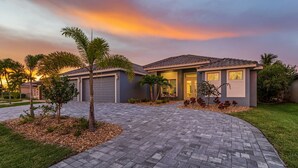 A residential house with a paved driveway, palm trees, and a well-maintained lawn. - GULF ACCESS & BIG WATER VIEW!, Heated Saltwater Pool  and Spa -  Villa Manatees Crossing - Roelens (Cape Coral)