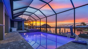 A swimming pool with a view of a sunset over water, surrounded by a covered area with a geometric roof structure. - GULF ACCESS & BIG WATER VIEW!, Heated Saltwater Pool  and Spa -  Villa Manatees Crossing - Roelens (Cape Coral)