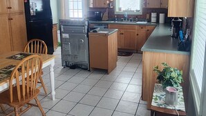 A kitchen with wooden cabinets, a refrigerator, a stove, and a dining area with chairs and a table. - Snowmobiling & Fourwheelering right out on the main trail (Stewartstown)