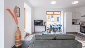 Una sala de estar moderna con un sofá gris, un televisor de pantalla plana y una zona de comedor con sillas azules y una mesa.