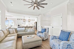 Ein geräumiges Wohnzimmer mit einer großen Eckcouch, einem gemusterten Sessel und einem Deckenventilator.