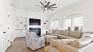 Ein modernes Wohnzimmer mit einer Couch, einem Sessel und einem Couchtisch, einem Fernseher und einem Deckenventilator.