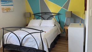 A bedroom with a bed, two bedside tables, a lamp, a wall art piece, and a white wardrobe. - Tiny house on an orchard (Oliver)