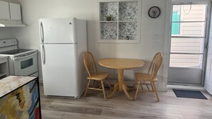 A kitchen with white appliances, a wooden dining table, and chairs. - Tiny house on an orchard (Oliver)