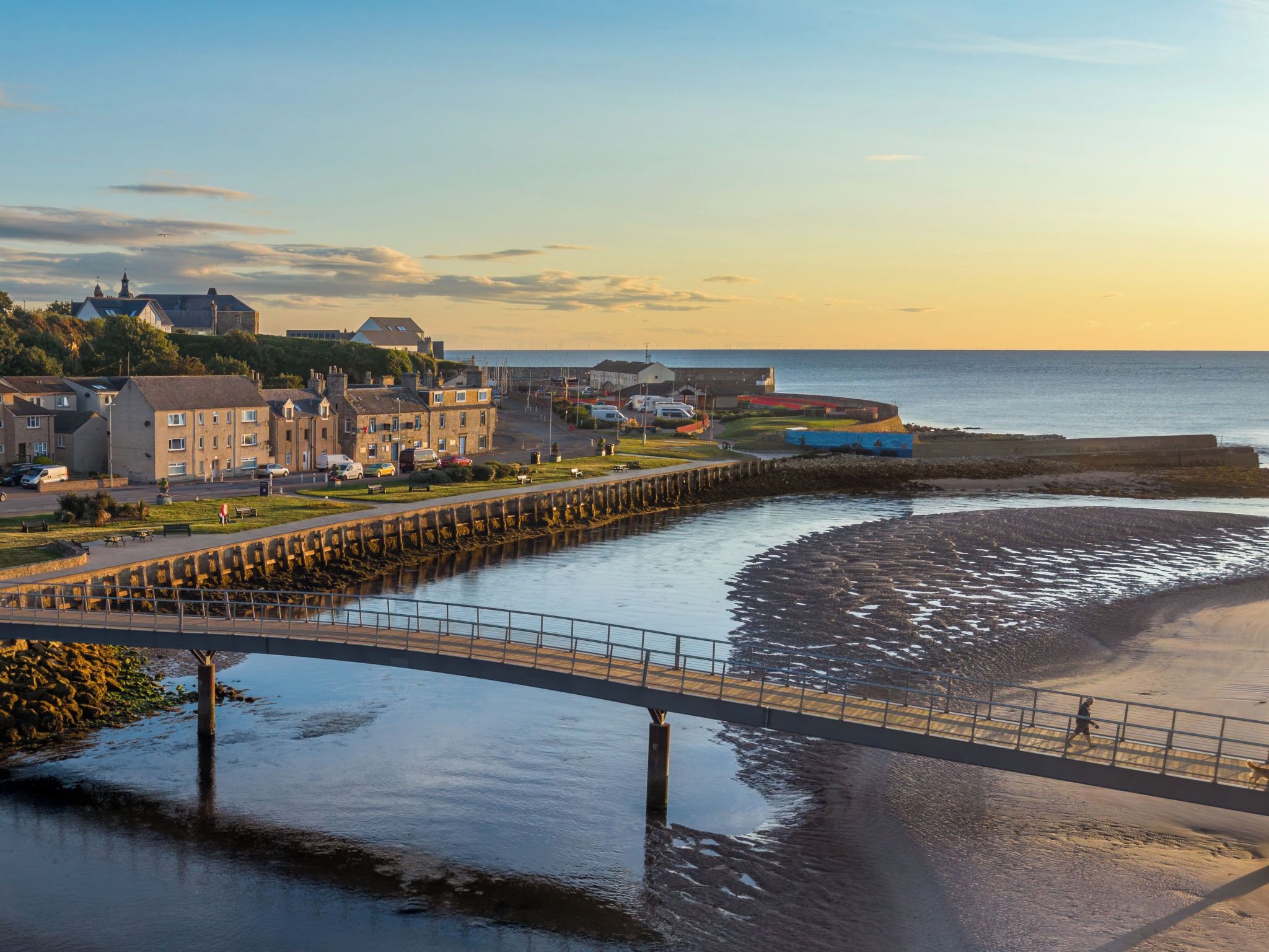 A coastal town with a bridge over a river leading to a beach.