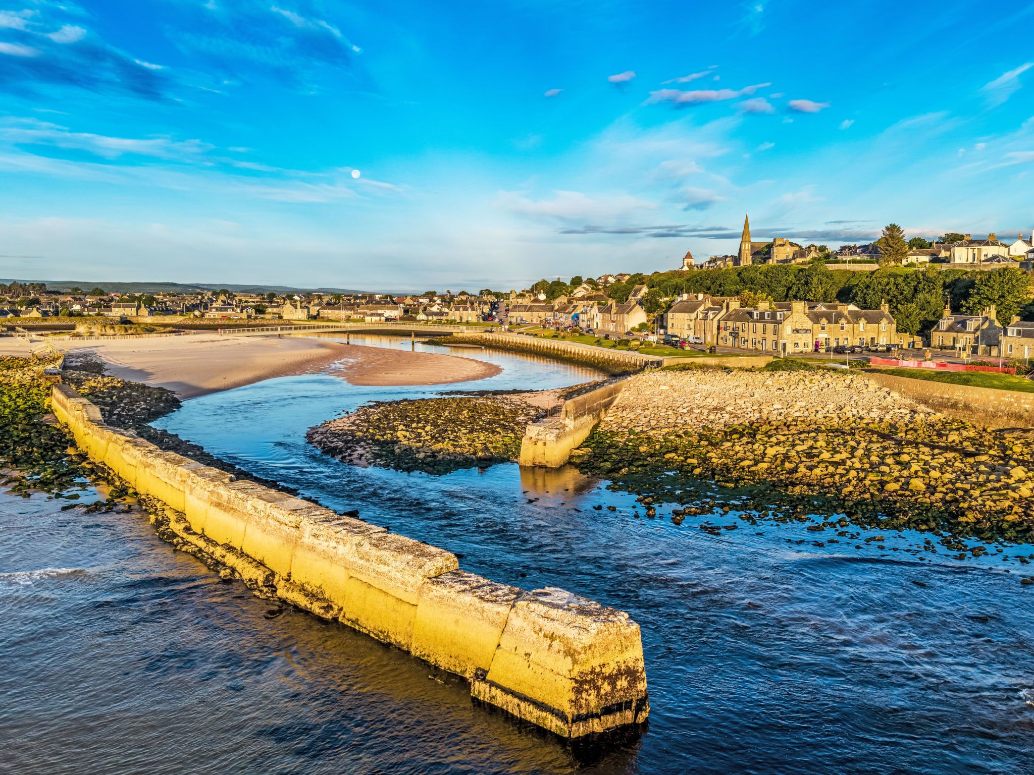 A coastal town with a prominent church, a sandy beach, and a stone sea wall.