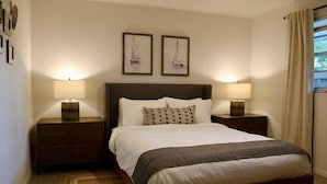 Un dormitorio ordenado con una cama grande, dos mesitas de noche con lámparas y dos cuadros en la pared.