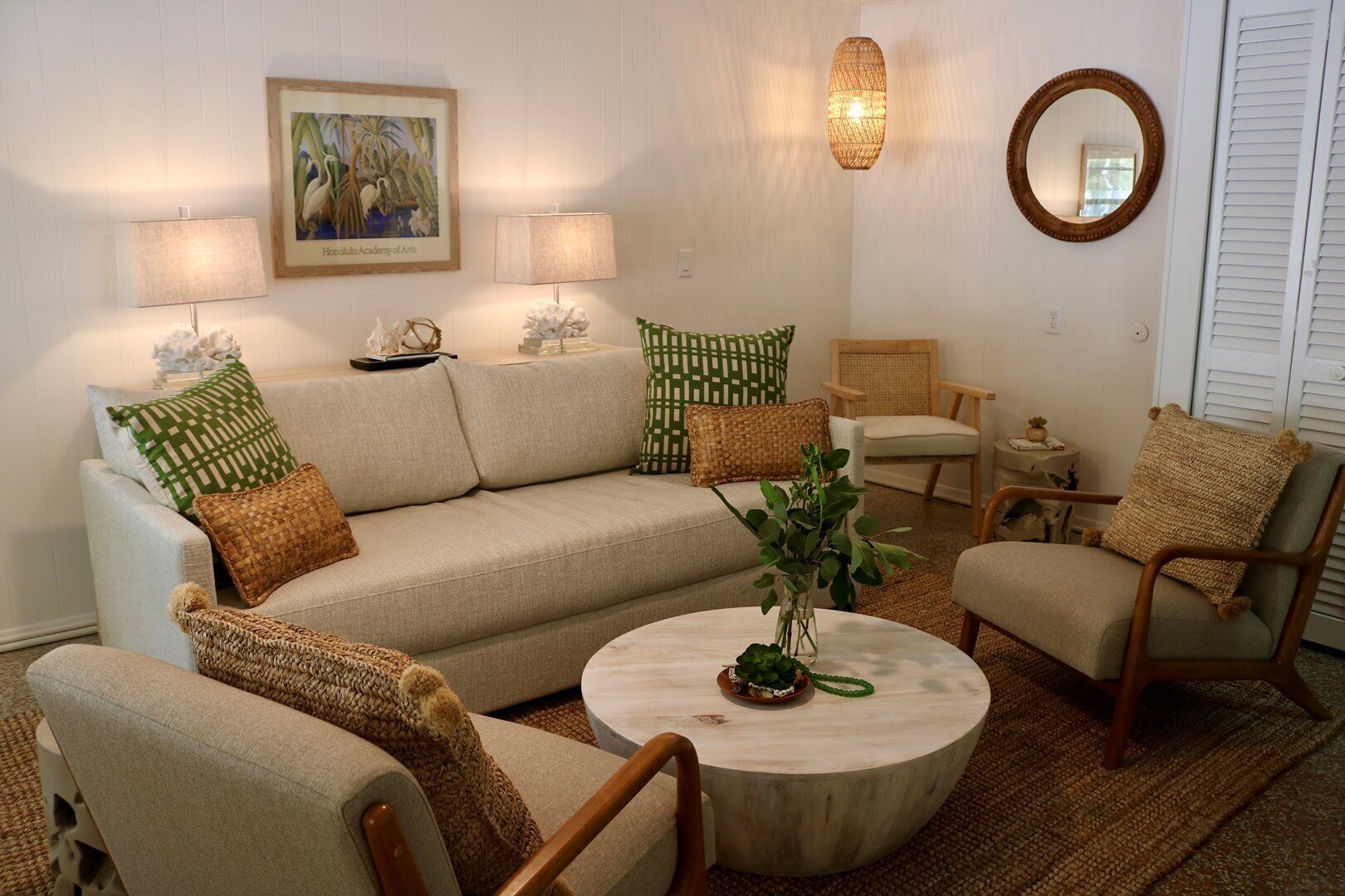 A living room with a sofa, two armchairs, a coffee table, a lamp, a mirror, and a framed picture on the wall.