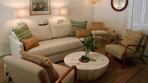 Una sala de estar con un sofá, dos sillones, una mesa de centro, una lámpara, un espejo y un cuadro en la pared.