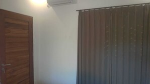 A room with a wooden door, a window with vertical blinds, and an air conditioning unit on the wall. - Keramas House (Gianyar)