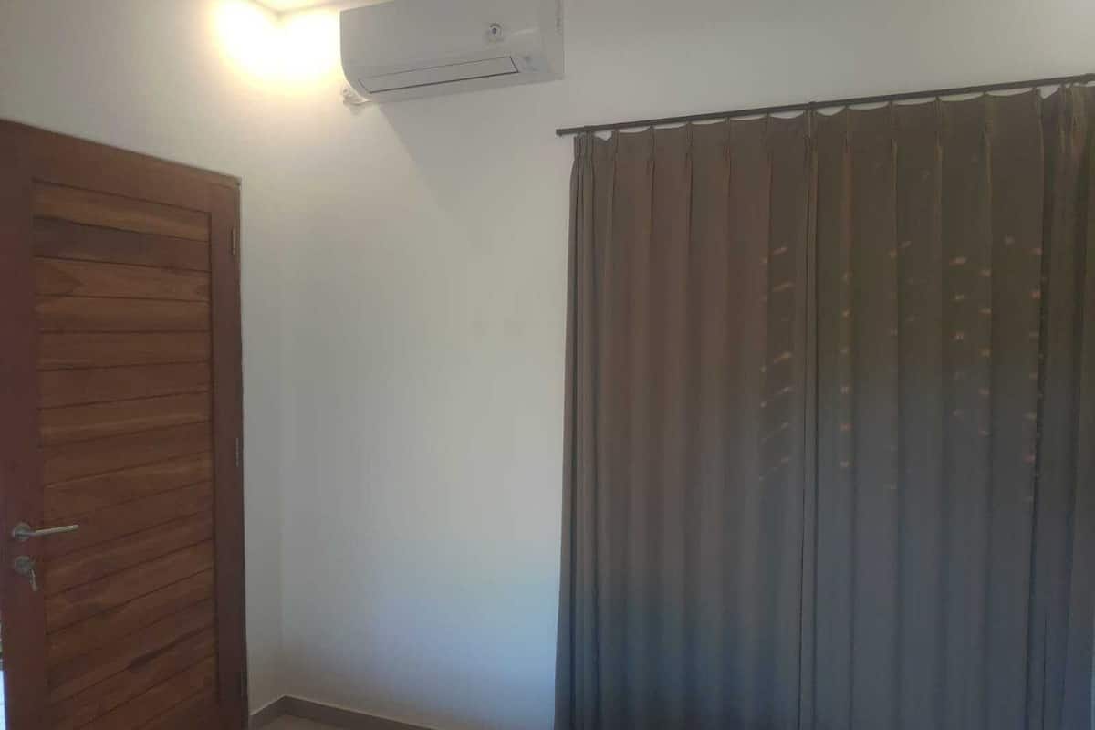 A room with a wooden door, a window with vertical blinds, and an air conditioning unit on the wall.