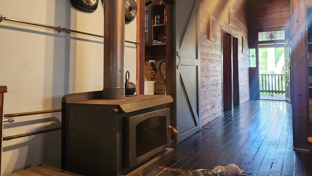 A rustic kitchen with a wood-burning stove, hanging pans, and a wooden interior. - Secluded rustic cottage charm, opposite river walk, close to town. Pet friendly! (Bridgetown)