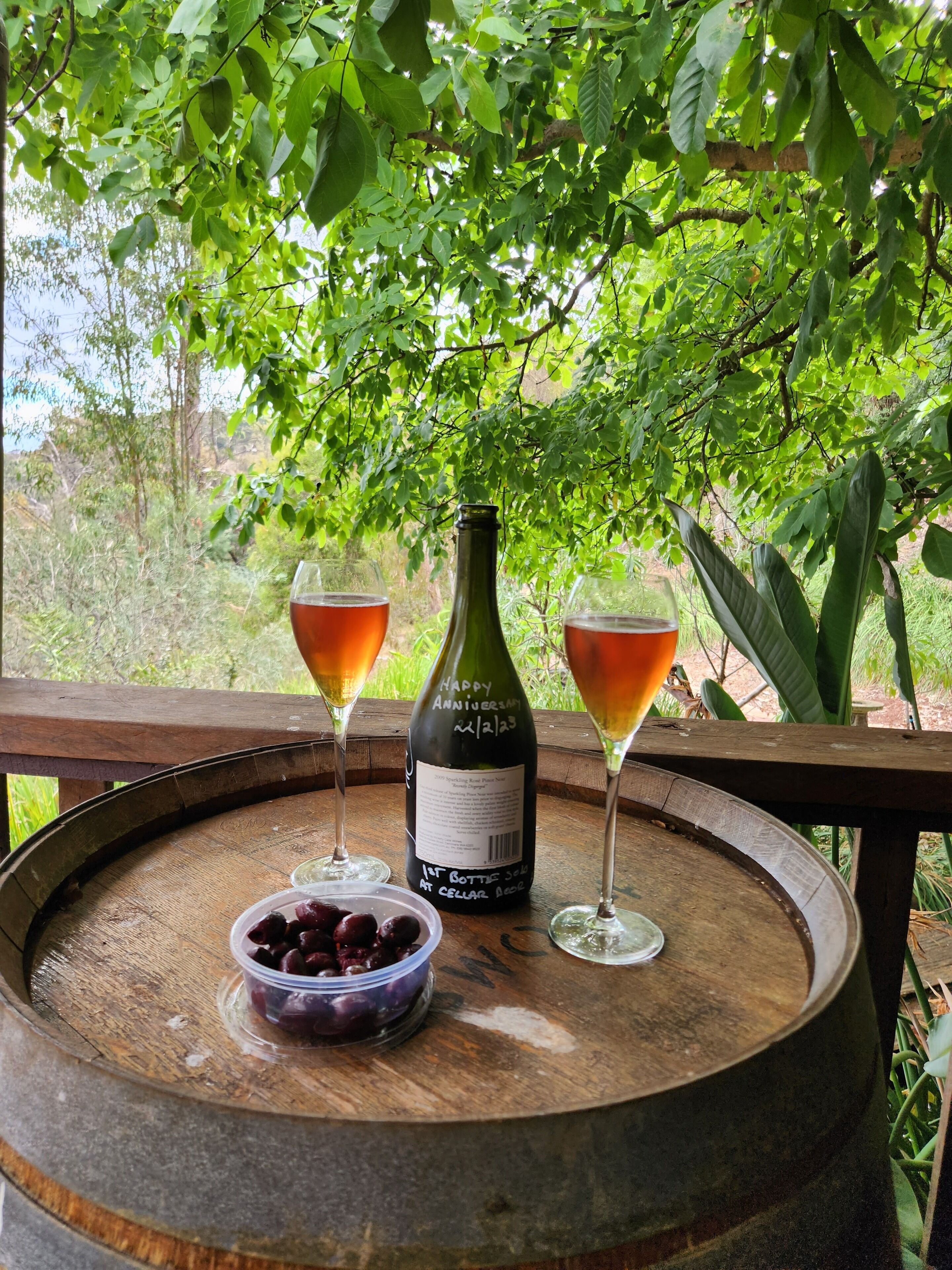 A wooden barrel with a bottle and two glasses of red wine, a bowl of cherries, and a wooden table.