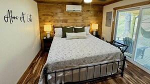 A bedroom with a bed, two bedside tables with lamps, a ceiling fan, and a sliding glass door leading to an outdoor area. - Alone At Last- Hot tub, Fireplace, Fire pit (Campton)