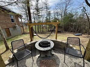 A circular outdoor seating area with a fire pit in the center, surrounded by two metal chairs and a wooden pergola overhead. - Alone At Last- Hot tub, Fireplace, Fire pit (Campton)