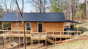 A log cabin with a metal roof, wooden deck, and a hot tub on the porch. - Alone At Last- Hot tub, Fireplace, Fire pit (Campton)
