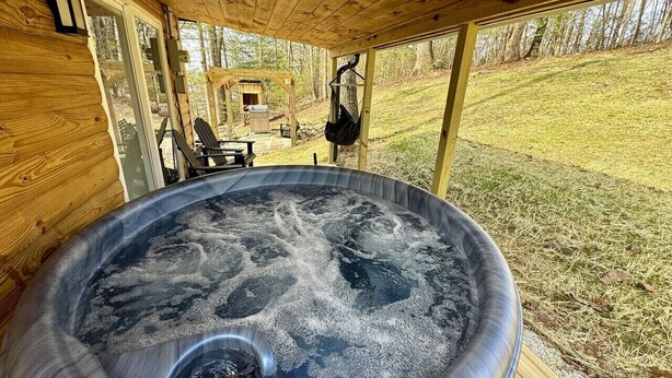 A hot tub in a wooden cabin with a view of the surrounding forest. - Alone At Last- Hot tub, Fireplace, Fire pit (Campton)