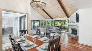 A spacious dining area with a wooden table set for a meal, a chandelier, and a view of the outdoors through large windows. - Single Level Home with Game Room and Putting Greens (Hilton Head Island)