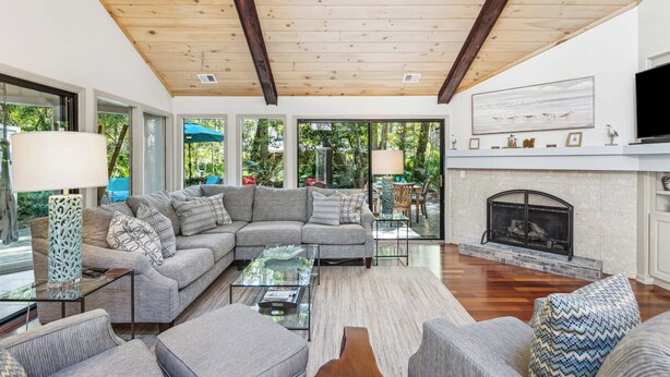 A spacious living room with a large sectional sofa, a fireplace, and a TV mounted on the wall. - Single Level Home with Game Room and Putting Greens (Hilton Head Island)