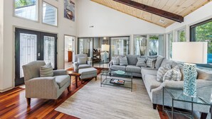 A spacious living room with a high ceiling, large windows, and a cozy seating area. - Single Level Home with Game Room and Putting Greens (Hilton Head Island)