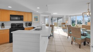 A modern kitchen with wooden cabinets, a large island, and a dining area with wicker furniture. - Beachfront condo with indoor and outdoor pools! (Hilton Head Island)