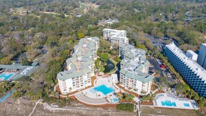 An aerial view of a resort with multiple buildings, a central pool, and surrounding greenery. - Beachfront condo with indoor and outdoor pools! (Hilton Head Island)