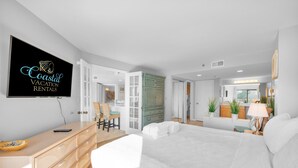 A modern bedroom with a bed, dresser, and a television displaying 'Coastal Vacation Rentals'. - Beachfront condo with indoor and outdoor pools! (Hilton Head Island)