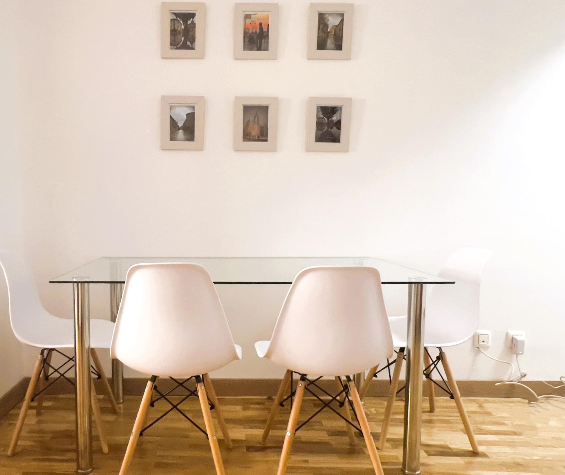 A modern dining area with a glass table and four white chairs with wooden legs.