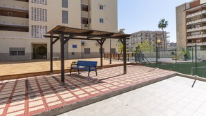 Une cour avec une pergola en bois, un banc bleu et un espace de jeux pour enfants.