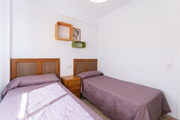 Ein Schlafzimmer mit zwei Einzelbetten, einem Holznachttisch und einem an der Wand befestigten Regal mit Bilderrahmen.