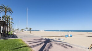 Une promenade en bord de mer bordée de palmiers, un ciel dégagé et une plage de sable en arrière-plan.