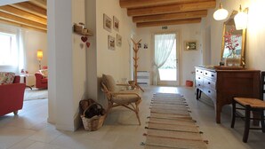 Ein gemütliches Zimmer mit Holzbalkendecke, einem roten Sessel, einem Korbstuhl, einem Holzschrank und einem Spiegel.