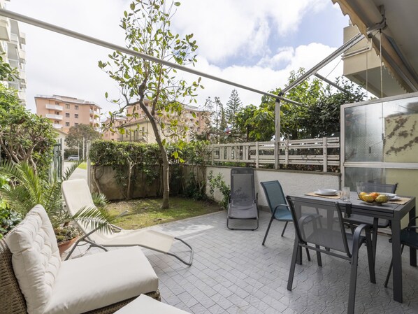 Un espace patio avec une table et des chaises, un fauteuil rembourré et une vue sur les bâtiments en arrière-plan.