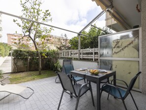 Une terrasse extérieure avec une table et des chaises, un petit jardin et une vue sur les bâtiments voisins.