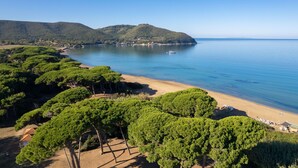 A coastal landscape with a beach, dense green trees, and hills in the background. - Sunset Populonia by Geco Vacation Rentals (Populonia)