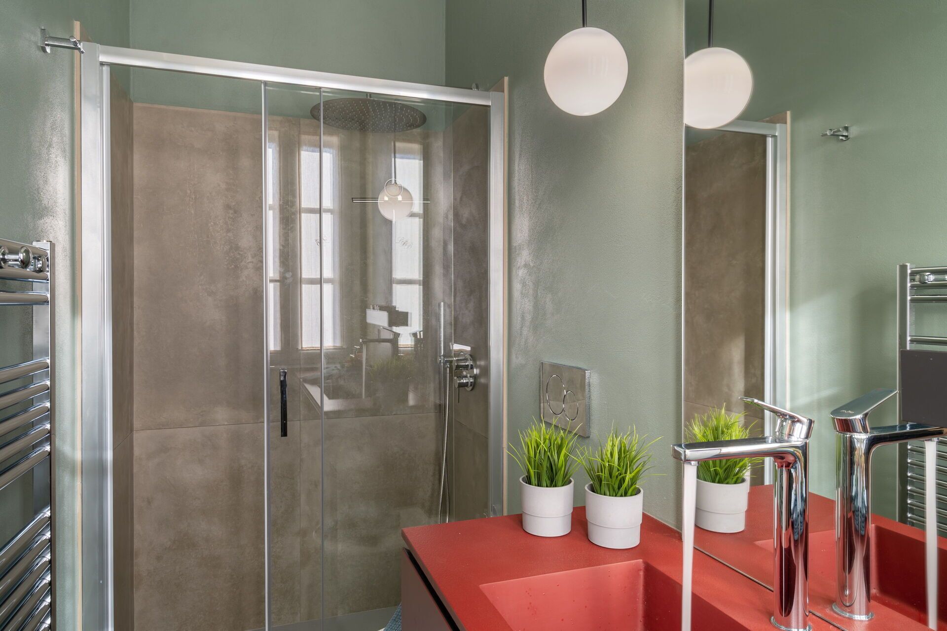 A modern bathroom with a glass shower enclosure, a red countertop, and two potted plants.