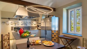 A modern kitchen with a stainless steel refrigerator, a wooden dining table with a basket, and a window with a view of greenery. - Sunset Populonia by Geco Vacation Rentals (Populonia)