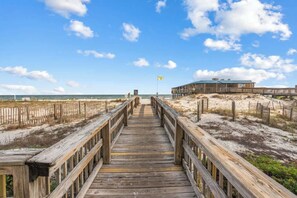 A wooden boardwalk leading to a beach area with a building in the background. - Boardwalk 584 (Gulf Shores)