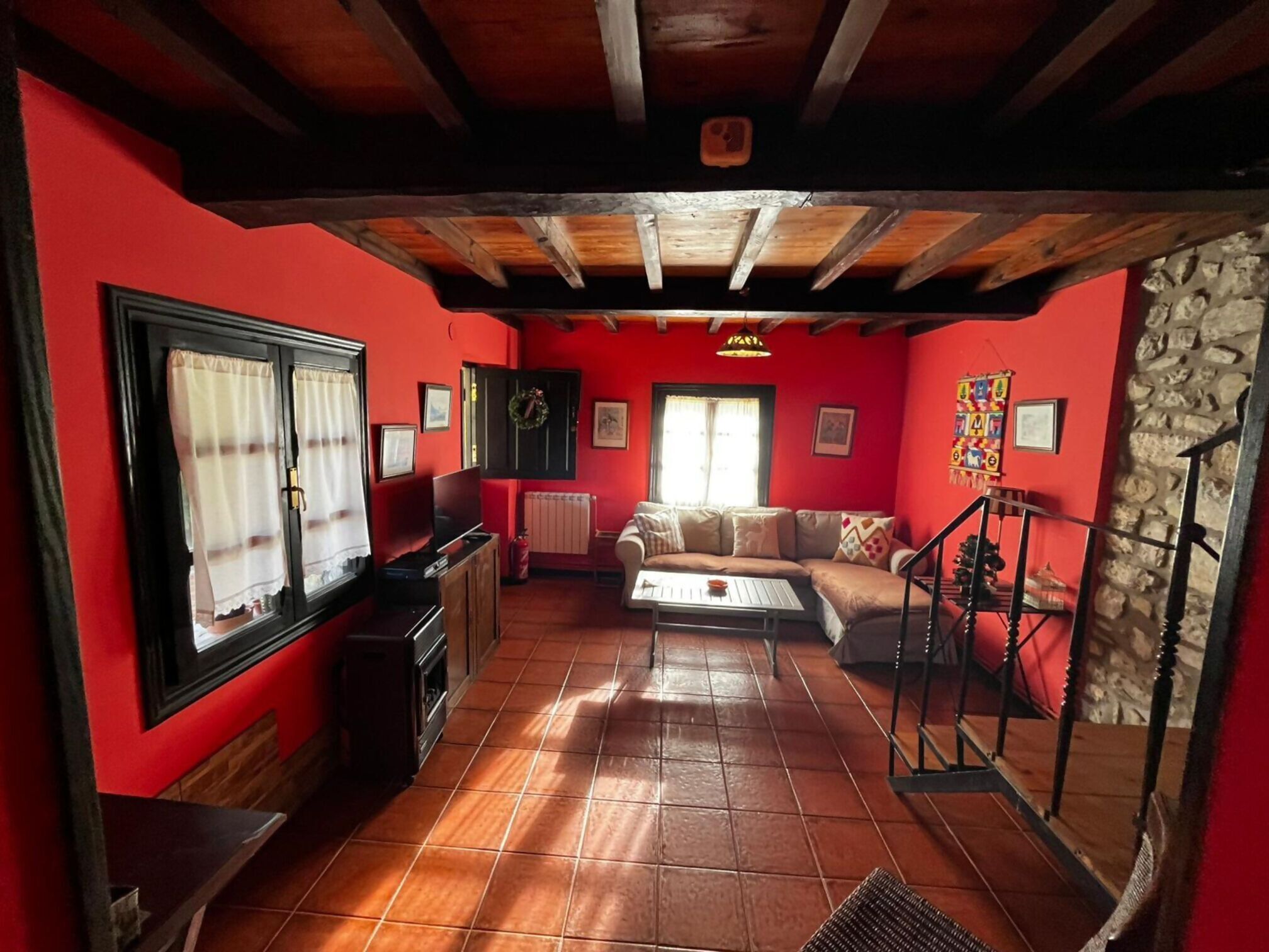Una sala de estar acogedora con pared roja, vigas de madera en el techo, un sofá, una mesa de centro y una pared de piedra.