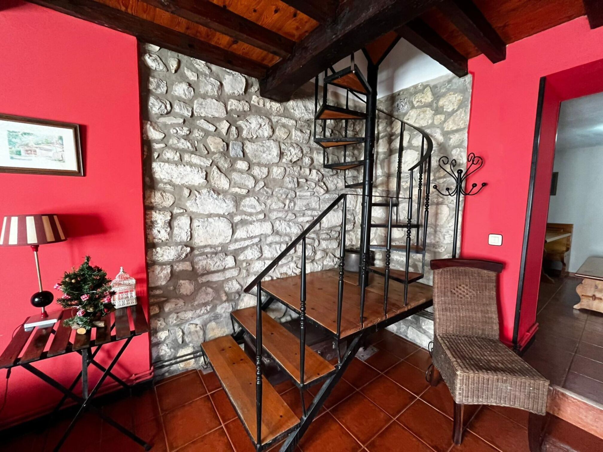 A staircase with a stone wall, a small table with a lamp, and a wicker chair.