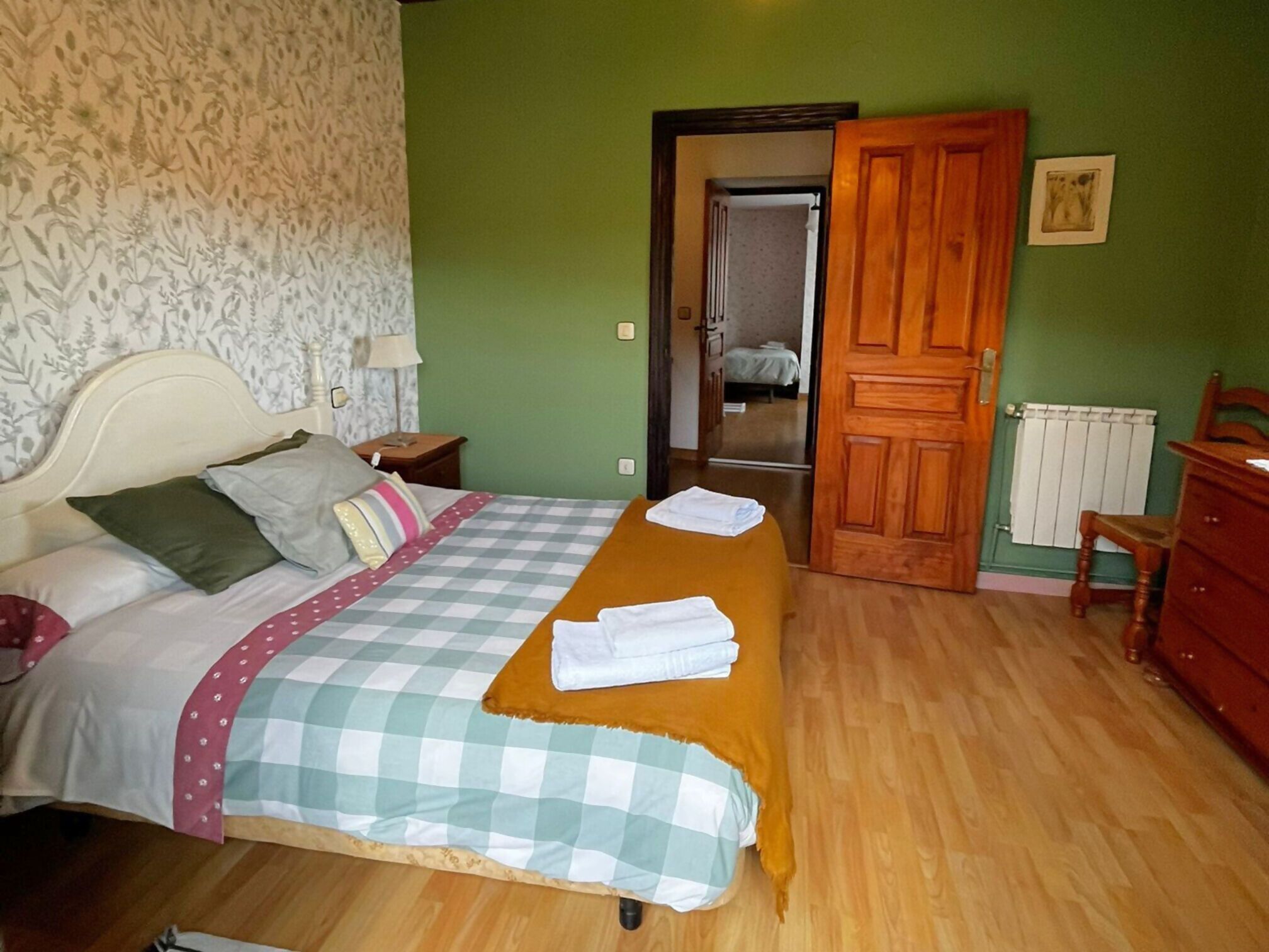 A bedroom with a bed, a wooden dresser, a radiator, and a door leading to another room.