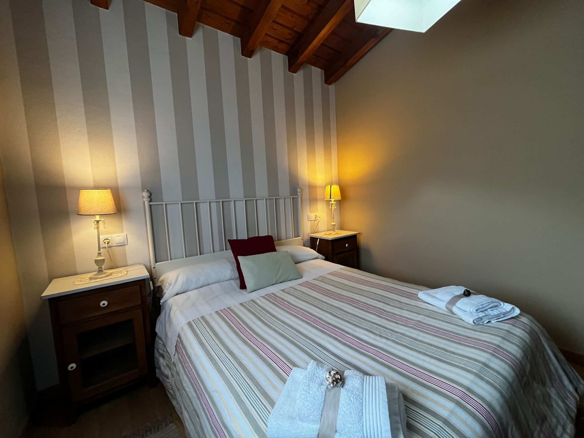 A hotel room with a striped wall, a bed with a striped bedspread, two bedside lamps, and a wooden headboard.