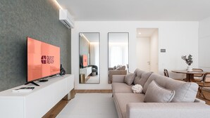 A modern living room with a flat-screen TV, a sofa, a dining table, and a large mirror. - GuestReady - Little Johnny Stay (Porto)