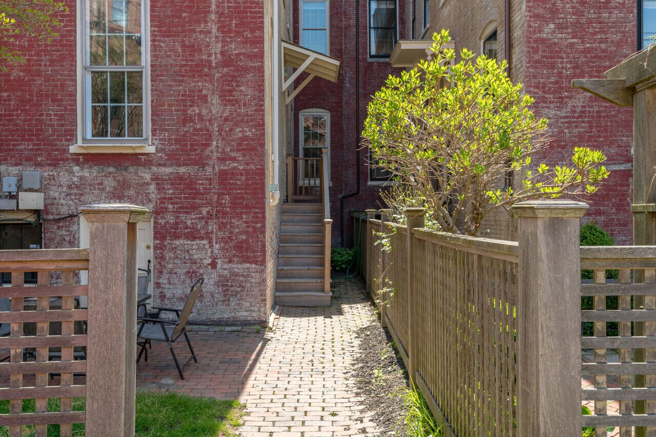 A brick building with a wooden fence, a paved pathway, and a small garden area.