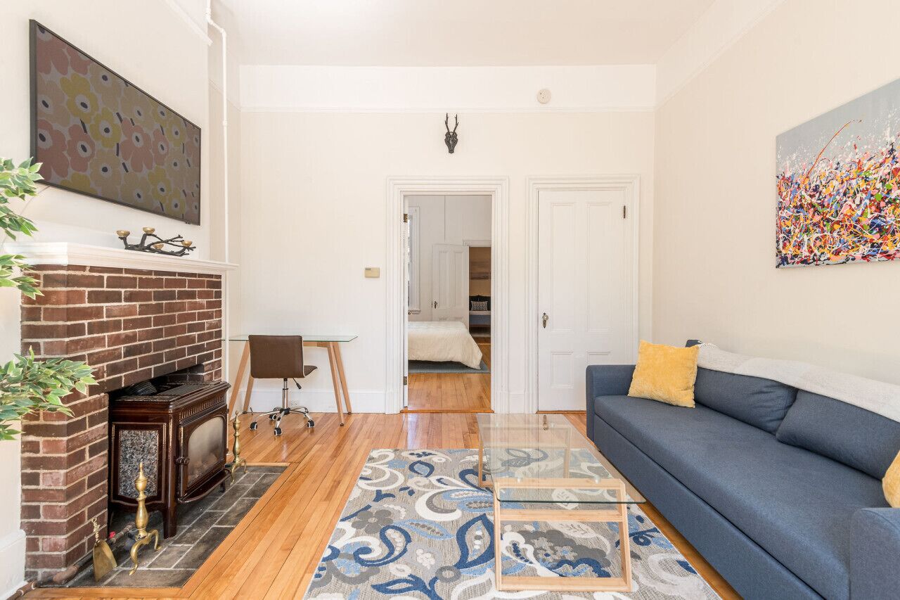 A living room with a fireplace, a blue sofa, a patterned rug, and a painting on the wall.
