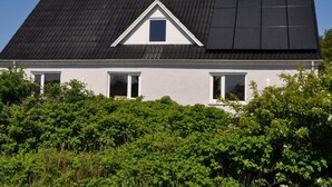 Una casa con techo inclinado, paneles solares y un pequeño ventanal triangular.