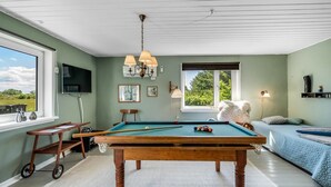 Una mesa de billar en una habitación con un ventanal grande, un televisor y una cama acogedora.