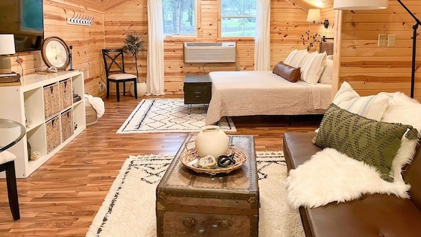 A cozy cabin interior with a wooden ceiling, a bed, a sofa, a small table, and a television. - The Dens at Bear Rock 2 with stairs access (Custer)