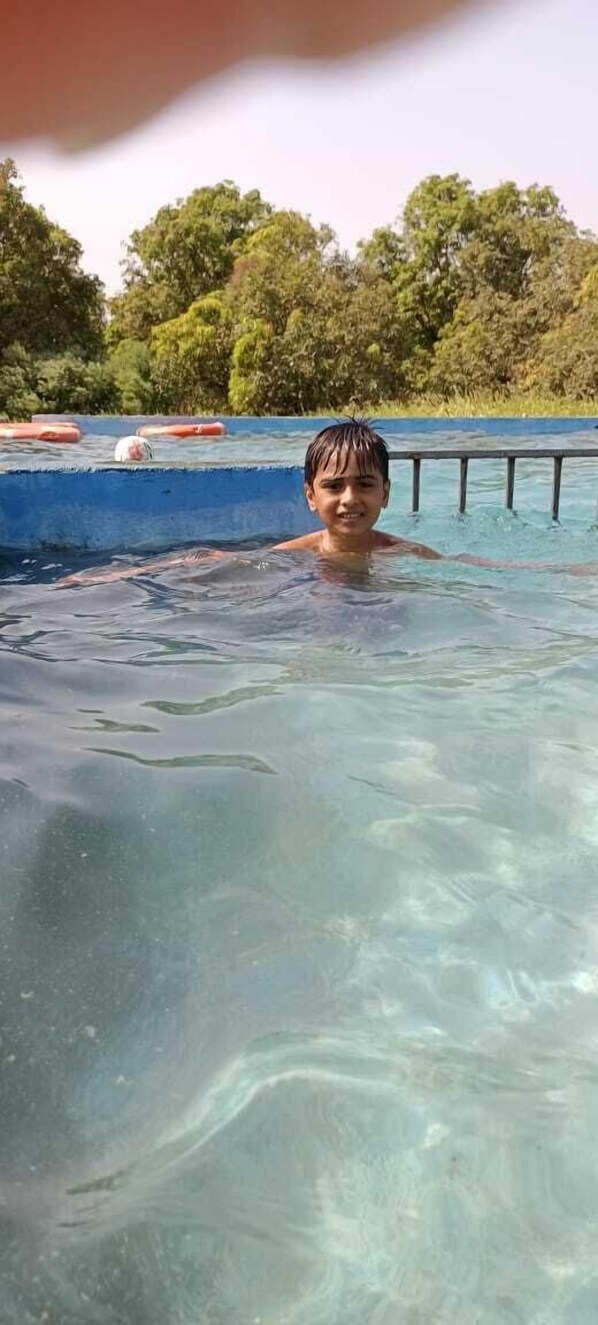 A person in a clear pool with a blue edge and floating barriers. - S R Farm House (Talala)